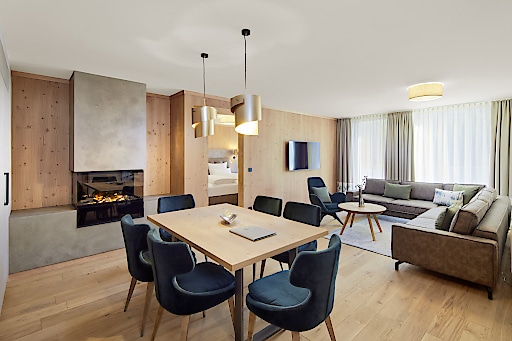 Neues Zimmer im Zugspitz Resort mit Kamin, Esstisch mit 6 Stühlen, großem Ecksofa und Flachbildfernseher an der Wand